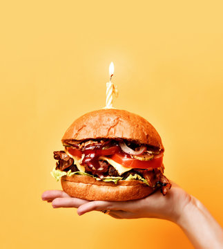 Woman hands hold big tasty burger barbeque sandwich with marble beef and lit candle for birthday party