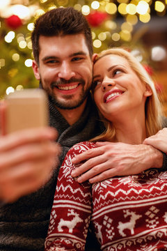 smiling woman and man in warm sweaters taking selfie picture with smartphone.