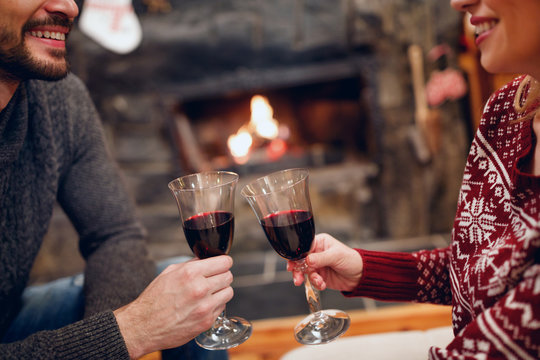couple toasting delicious red wine at romantic fireplace.