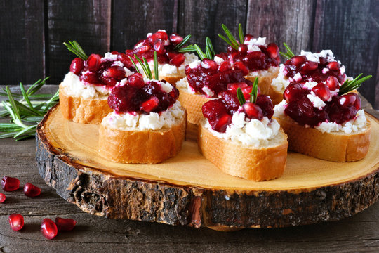 Holiday crostini appetizers with cranberries, pomegranates and feta cheese on a rustic wood platter