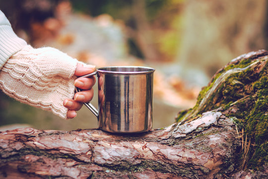 Woman with knitted glove is holding metal mug with drink. Refreshment during hiking. 