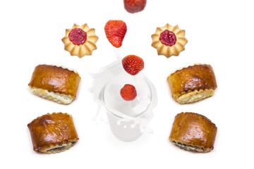 strawberry falling into a glass of milk with splashes around which are tasty cookies