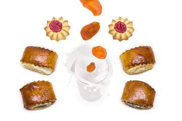 dried apricot falling into a glass of milk with splashes around which are tasty cookies