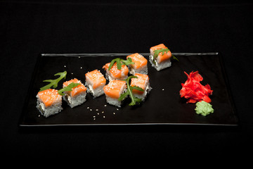 Sushi roll with salmon and avocado on plate on black background top view