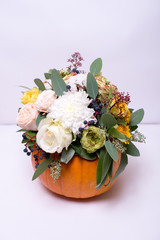 Autumn floral bouquet in a pumpkin vase on a light background, a mixture of flowers, pionic rose, eucalyptus, chrysanthemum