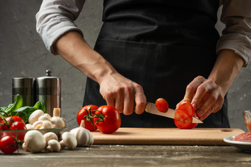 The concept of nutrition. The chef cuts tomatoes close-up, against the background of a concrete...