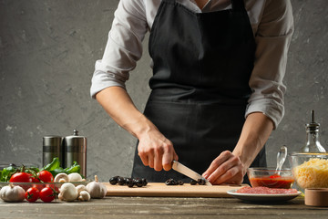 The concept of nutrition. The chef cuts olives on the background of a concrete wall, with...