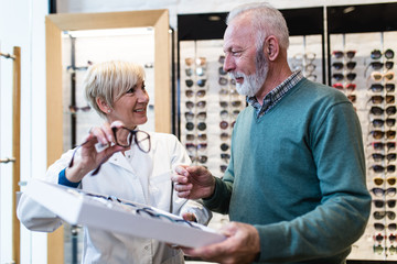Handsome senior man choosing eyeglasses frame in optical store.