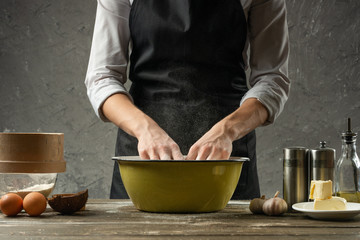 Chef preparing the dough. A low key shot, some ingredients on the table. Against the background of the concrete wall, with empty space, the concept of cooking pizza, pasta, bread, dough