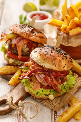 Homemade burgers with grilled bacon, red onion, fresh lettuce, cucumber pickles, tomato and aromatic mayonnaise sauce on a wooden board. 
