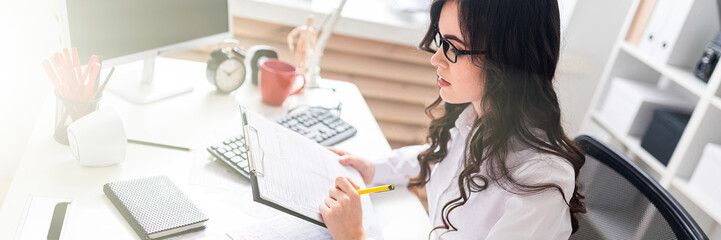A young girl sits at the office desk and checks documents.