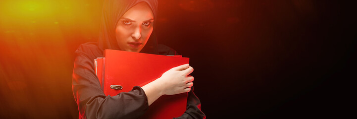 Portrait of woman holding folders against black background