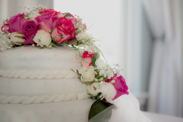 beautiful white wedding cake decorated with roses and natural light as background