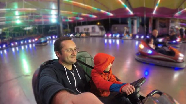 Child driving together with his father a car in amusement park, night fun 