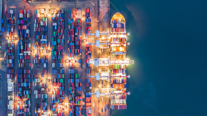 Aerial top view crane shipping container at night, cargo container ship carrying container import...