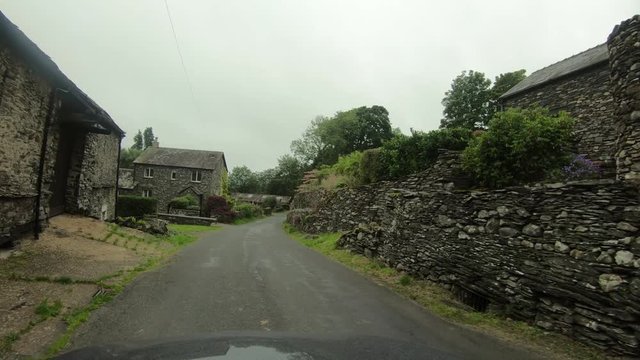 England drive POV narrow country road old houses. Historic old stone and rock homes along narrow winding roads. Northern England in Lake District National Park. Village of Windermere countryside.