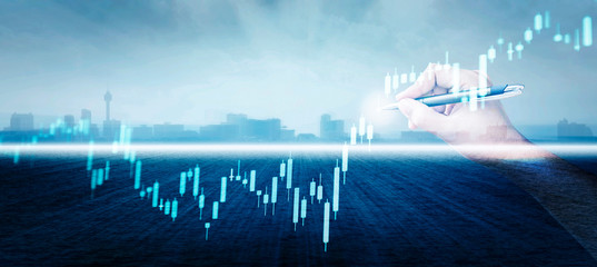 hand with a pen are sketching candle stick graph line with skyline cityscape and sea background