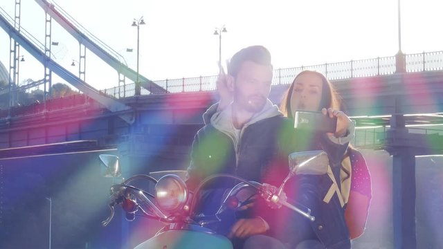 Couple on a scooter make selphie photos near the bridge.