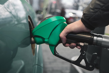 A man pours gasoline into the gas tank of a car. In his hand a green fuel nozzle.