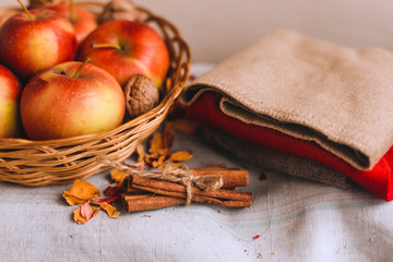 Still life with apples in a wicker basket, cloth, walnuts, flower petals and cinnamon sticks wrapped in twine. Concept of fall or winter home comfort.