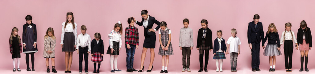 Obraz premium Cute smiling happy stylish children and female teacher on pink background. Beautiful stylish teen girls and boy standing together and posing at studio. Classic style. Kids fashion and emotions concept