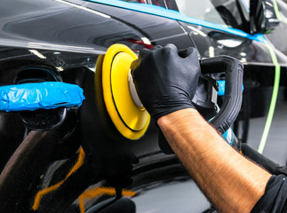 Car polish wax worker hands applying protective tape before polishing. Buffing and polishing car. Car detailing. Man holds a polisher in the hand and polishes the car