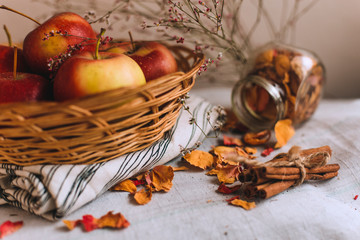 Still life with cinnamon sticks wrapped in twine, apples in a wicker basket stand on a striped linen cloth, walnuts and flower petals. Concept of home comfort in autumn or winter.