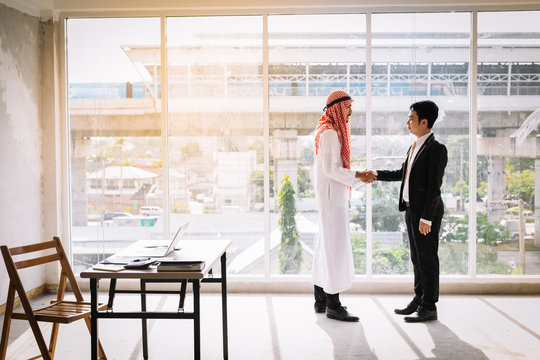 Arab and Asian business partners stand together after successful business talks.Two businessmen shake hands together as greetings congratulate each other.