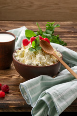 Cottage cheese with wooden spoon on it and milk in clayware on wooden table