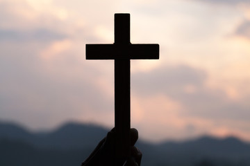 Woman hand holding holy lift of christian cross with light sunset background.
