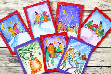 New Year (Christmas) cards with funny houses drawn in watercolor on a wooden background. Top view. Flatlay