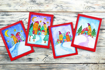 Fototapeta na wymiar New Year (Christmas) cards with funny houses drawn in watercolor on a wooden background. Top view. Flatlay