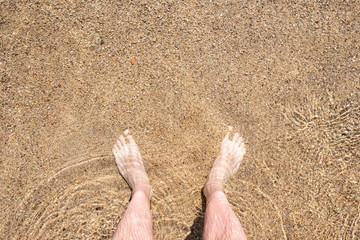 Foot on the beach. Top view of man legs on the water