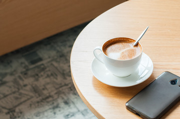 Cup of coffee and smartphone on a working table. Copy space, horizontal view.