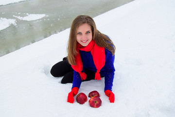 The young beauty the blonde placed red apples on snow. The woman is dressed in red knitted woolen gloves, a scarf, a blue sweater. The woman is in the winter park