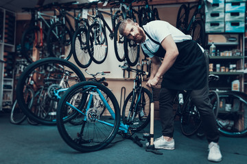 Fototapeta na wymiar Guy Pumps Bicycle Wheel with Air in Bike Workshop