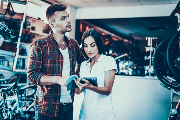 Young Couple Choose Bike Look at Catalog in Shop