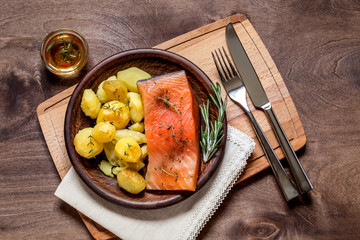Salmon fish with baked potatoes on a plate on a cutting Board on a brown wooden background