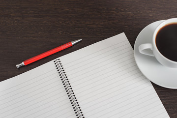 Notebook with pen and cup of coffee on brown wooden table