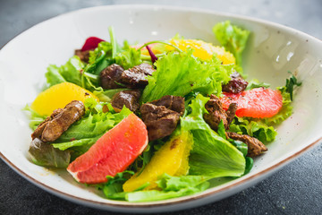 Tasty salad with citrus, lettuce and grilled chicken liver in a plate. Close up view