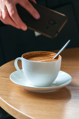 Close up of cup of coffee, woman holding her smartphone on backg