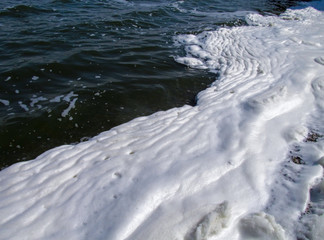 A lot of foam along the shore created by waves of water, close-up view. Summer scene of a lake or river. Concept of pollution of nature and a ecology problems of the environment.