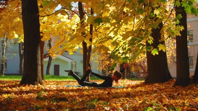 Pan shot. Young attractive woman doing yoga exersices in the park - bow pose. Golden autumn
