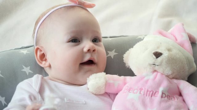 Close-up of little baby girl with toy bear ooks at camera and smiles.