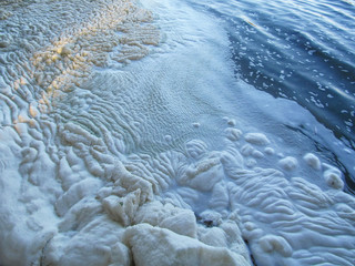 A lot of foam along the shore created by waves of water, close-up view. Summer scene of a lake or river. Concept of pollution of nature and a ecology problems of the environment.