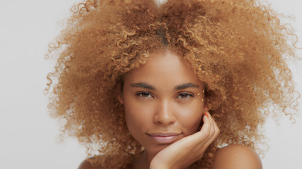 mixed race black blonde model with curly hair mith hand holding head watching to the camera