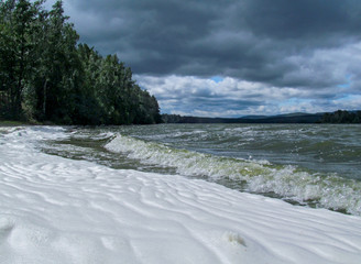 View of the lake from the beach, covered with a large surface of white foam. Unusual summer water landscape. Concept of pollution of nature and a ecology problems of the environment.