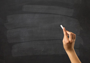 Female hand holding white chalk in front of a blank blackboard - obrazy, fototapety, plakaty