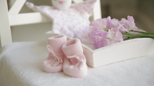 Little pink booties for newborn baby on background of flowers and toys. Concept of pregnancy and birth of girl