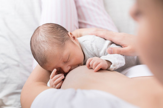A young mother breastfeeding her newborn baby boy while holding in her arms at bedroom at home.
